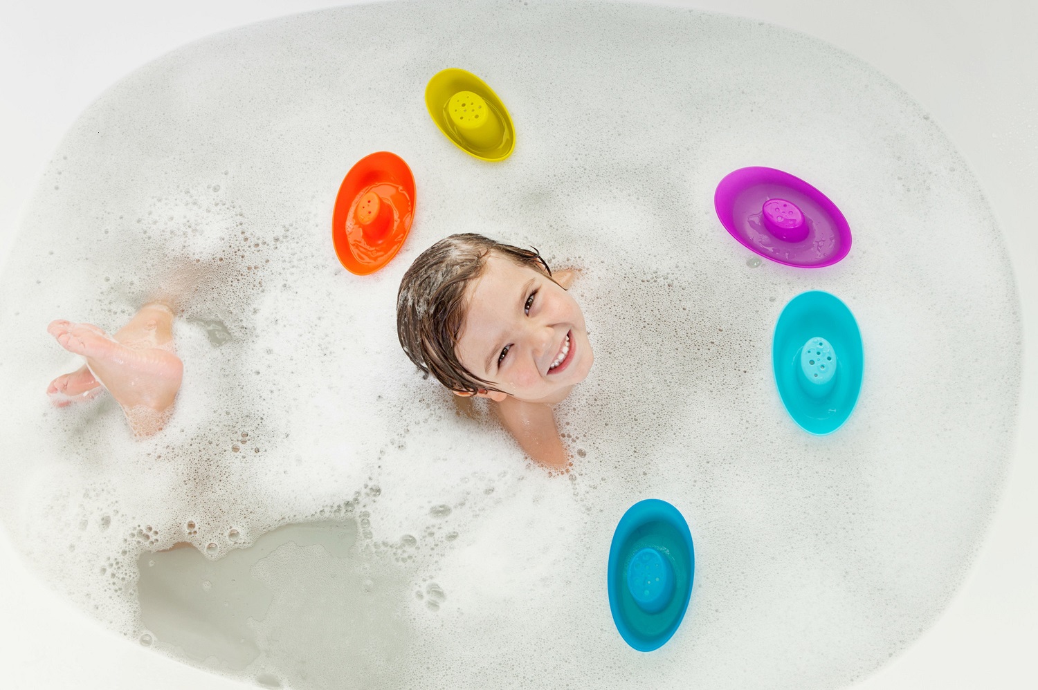 малыш в ванной, вид сверху, вокруг плавают разноцветные лодочки